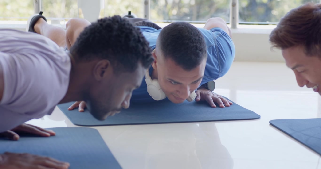 Diverse male group following blue shirt lead holding plank on mats in gym high-fiving and lowering
