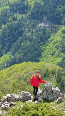 vertical aerial footage of a girl climbing rocky terrain in the balkan mountains near beklemeto pass. spring landscape, blue sky, and scenic views captured in daylight.