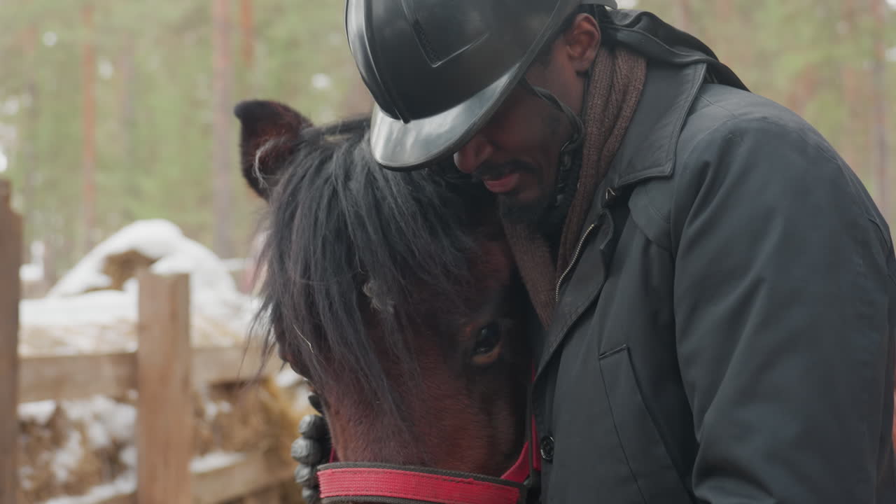 Terapeuta equina de piel oscura abrazando a un poni en un cercado de invierno, cálido abrazo y contacto frontal, cabestro rojo visible, bosque y nieve alrededor, momento de curación emocional y profunda conexión animal