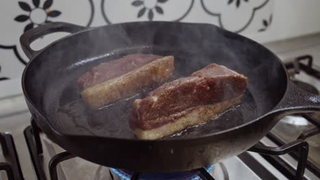 two seasoned meat steaks being grilled in hot pan