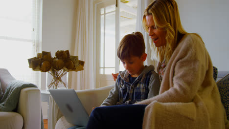 vista frontal de una joven madre y hijo caucásicos usando una computadora portátil en un sofá en un cómodo hogar 4k