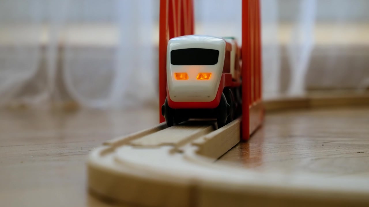Binari del trenino in legno con trenino giocattolo e ponte rosso sul pavimento