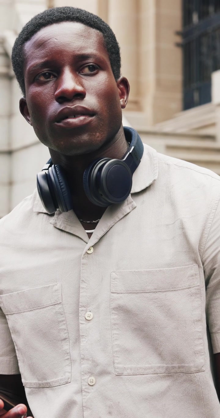 Giovane uomo che usa lo smartphone all'aperto con le cuffie intorno al collo