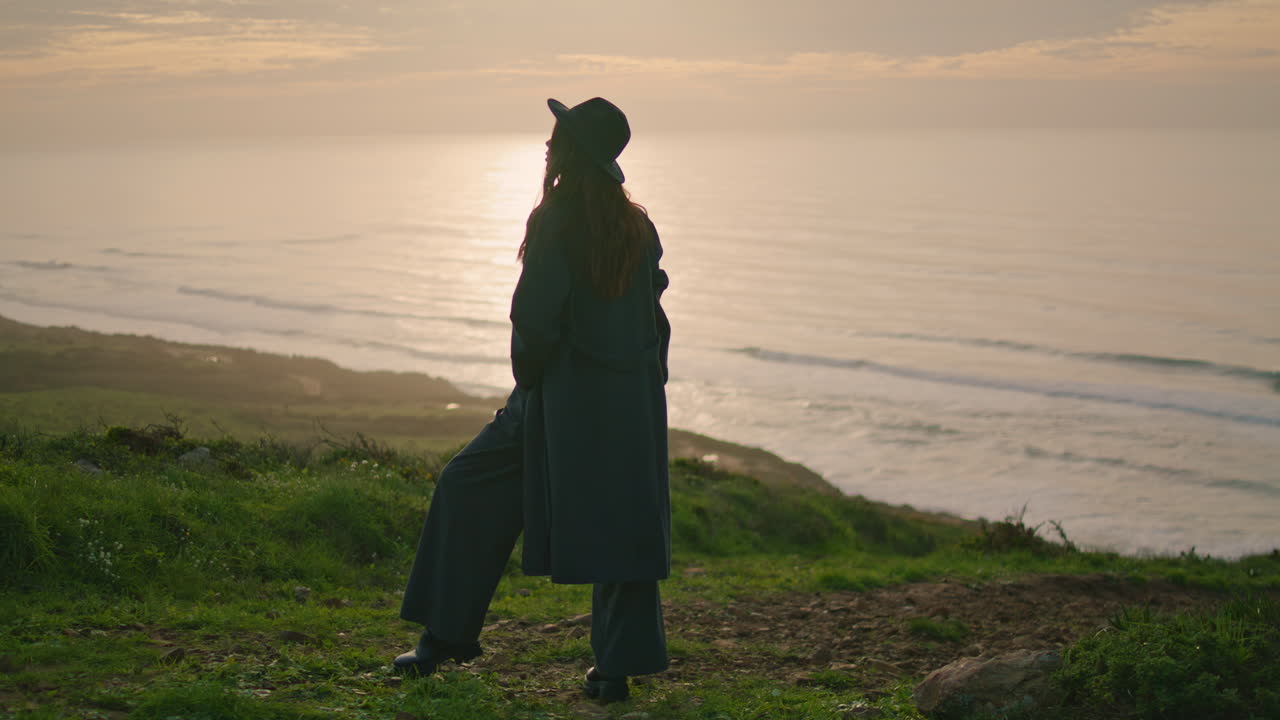 Silhouette di donna in piedi al tramonto sulla riva del mare. Ragazza elegante che posa nella natura.