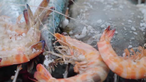 tongs flipping orange shrimp grilling on an outdoor bbq with fish, close up