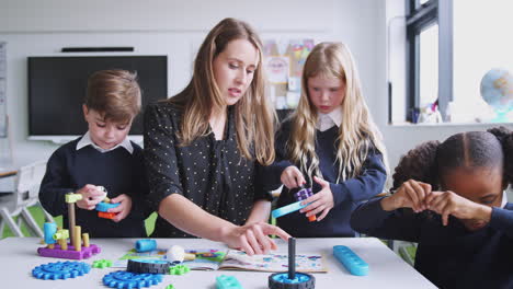 Female-teacher-helping-kids-working-with-construction-blocks-in-a-primary-school-classroom