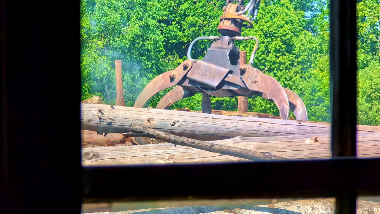 A Window With A View Of A Tractor-mounted Loader Lifting A Stack Of Logs. Close-up Shot