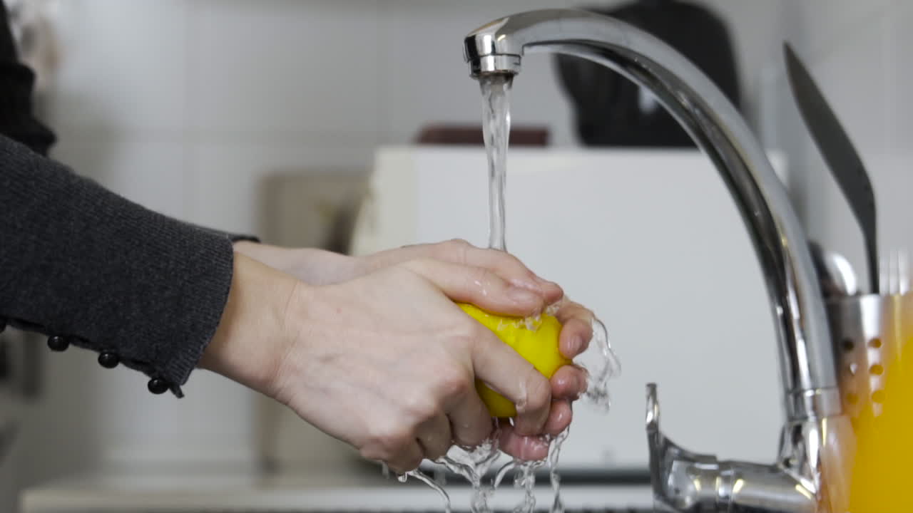 manos lavando un limón amarillo con agua del grifo en la cocina sobre el fregadero