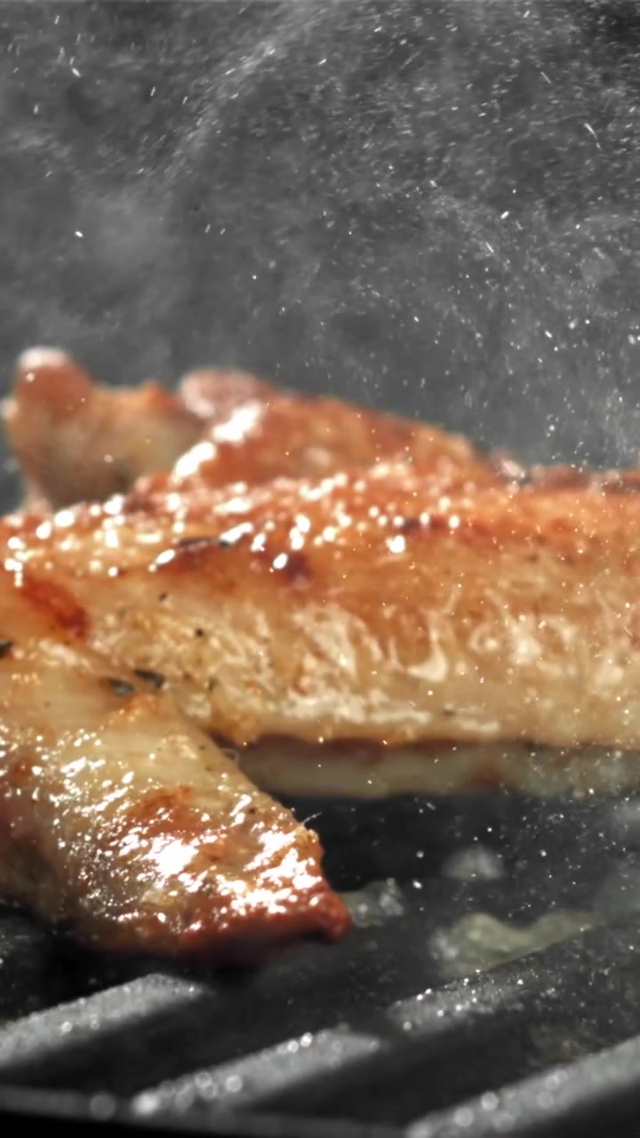 Slowmotion nærbillede af en kyllingevinge, der syder på en varm grill