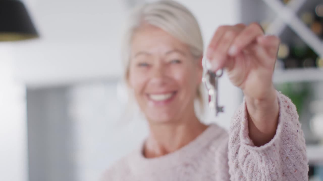 retrato de una feliz mujer caucásica mayor moviéndose de casa, sosteniendo las llaves en la cocina