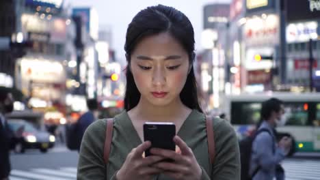 woman using phone in a busy city street at night
