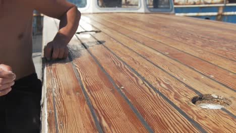 young man sanding timber on wooden boat by hand