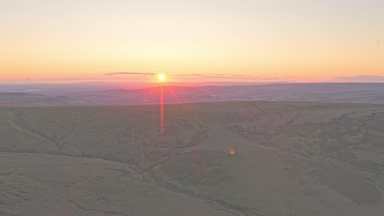Drone rises above the hill of Peak District, UK. Revealing an expansive landscape glowing under a stunning sunset