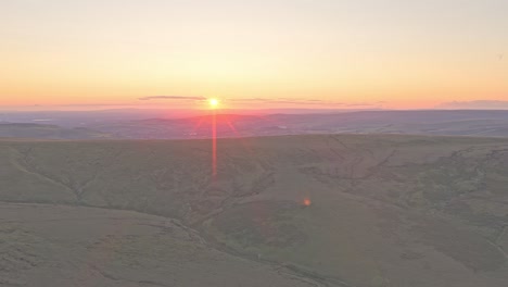 drone rises above the hill of peak district, uk. revealing an expansive landscape glowing under a stunning sunset