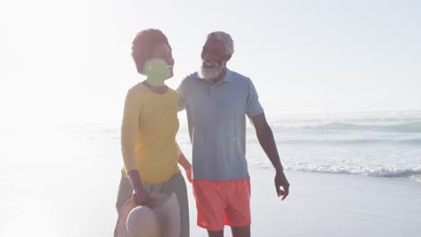 happy african american couple walking and talking on sunny beach