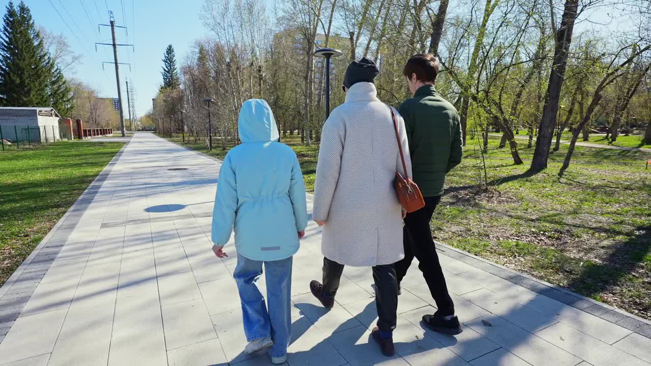 Three People Walking on a Paved Path in a Sunny Park