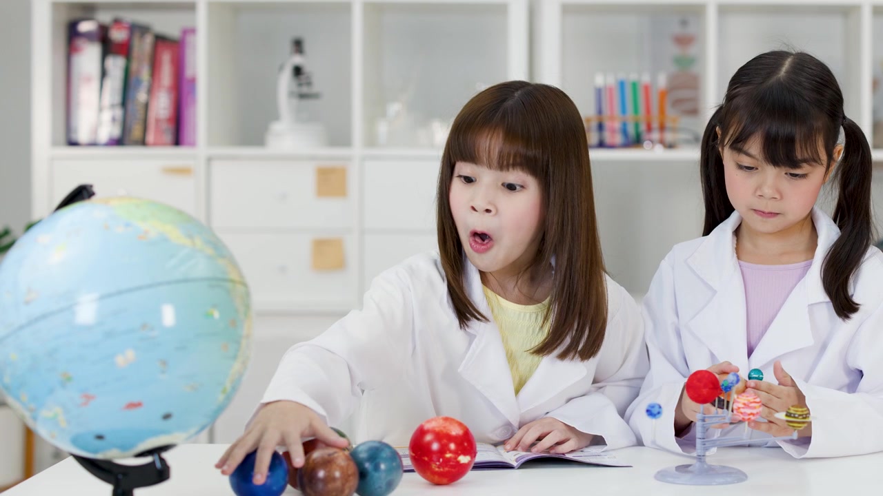 理科の授業で白衣を着た2人の若い生徒が惑星モデルと地球儀を調べる