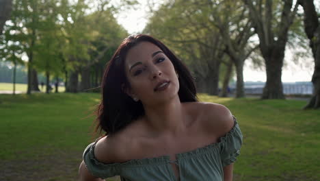 Slow-Motion-Portrait-of-a-gorgeous-hispanic-latino-young-woman-looking-at-the-camera-and-show-emotions-from-serious-to-smiling-and-laughing-with-a-beautiful-British-park-in-the-background