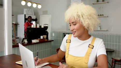 young biracial woman with curly blonde hair works on her laptop in a cafe