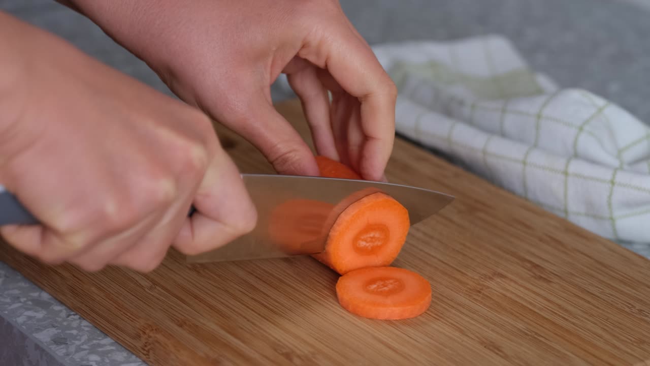 Woman cutting orange carrot on a wooden cutting board.