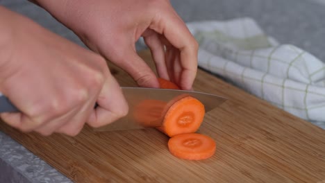 mujer cortando zanahoria naranja en una tabla de cortar de madera.