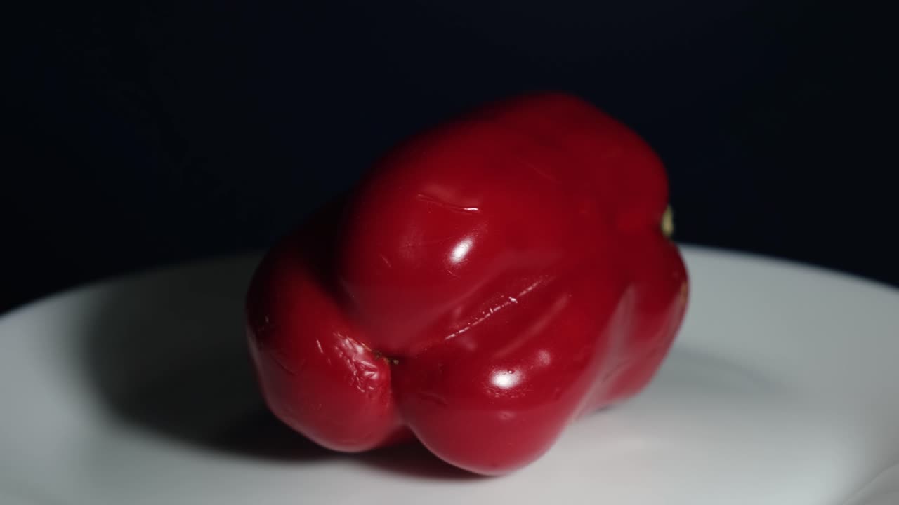 Red Bell Pepper turning around to the left while placed on a while porcelain plate
