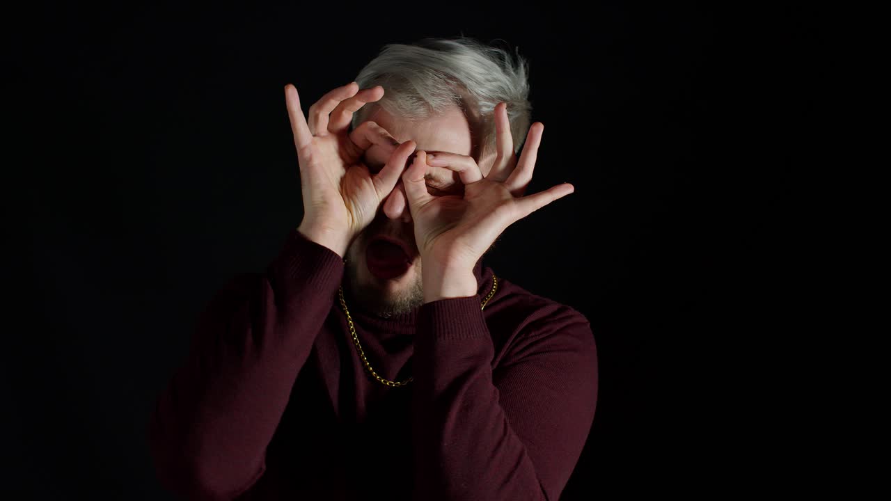 Cheerful funny man making glasses shape with hands, does funny silly face with eyes wide open