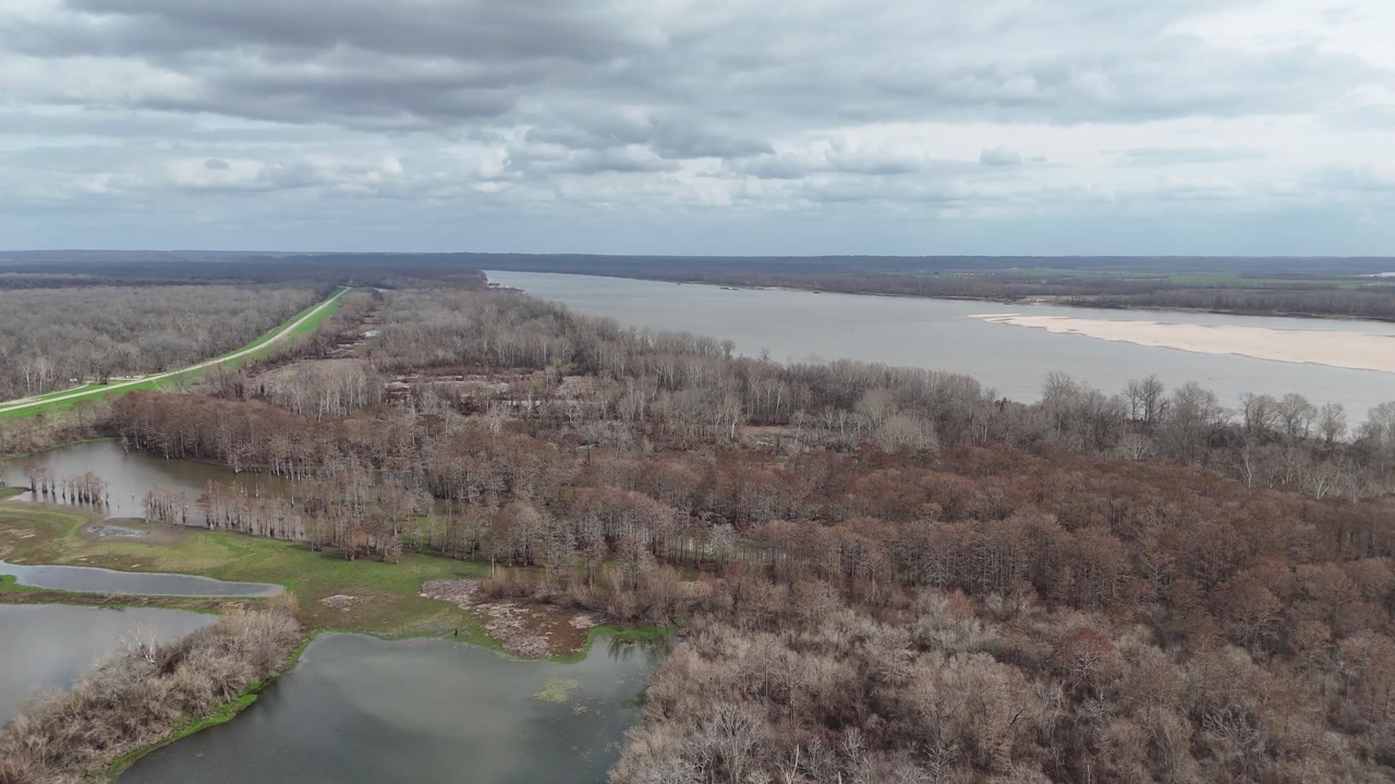Stunning aerial view showing the mighty mississippi river flowing beside a leafless winter forest and swamplands under a vast, cloudy sky, capturing the raw beauty of the american landscape