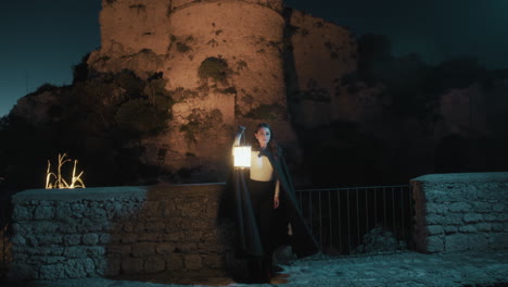 woman with cloak and lantern explores a medieval castle at night