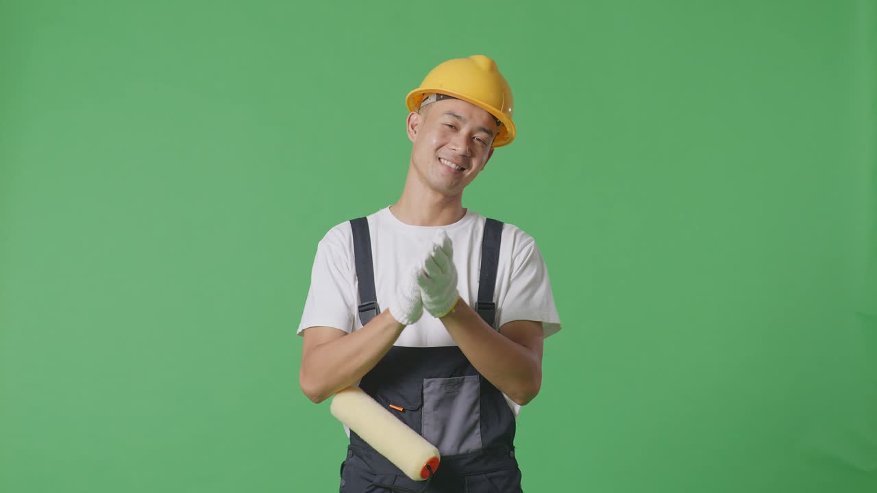Asian Man Painter Wearing Safety Helmet Smiling And Clapping His Hands While Standing In The Green Screen Background Studio