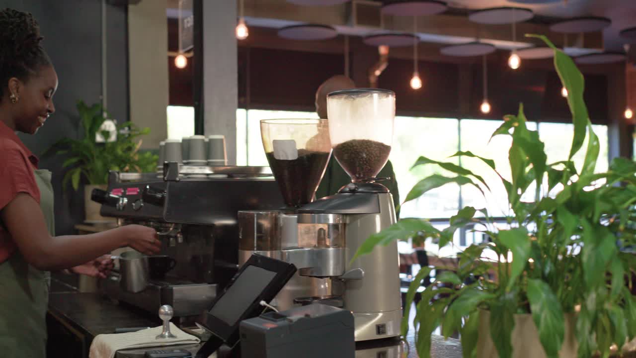 Barista afroamericano che prepara il latte sulla macchina da caffè espresso dopo che un uomo ha ordinato, consegnando la tazza e ricevendo il pagamento