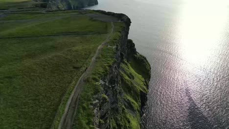 drone shot of the cliffs of moher at sunset, while hikers move along the cliffs