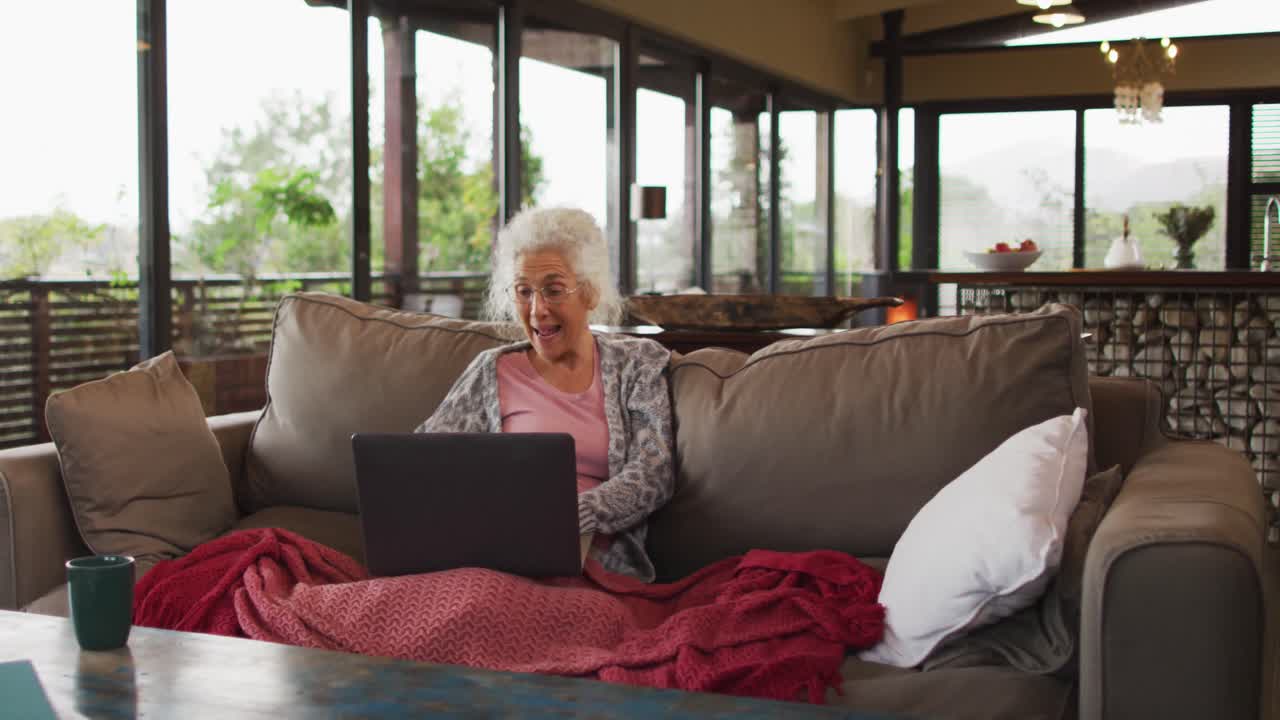 Senior mixed race woman sitting on sofa having video call using laptop