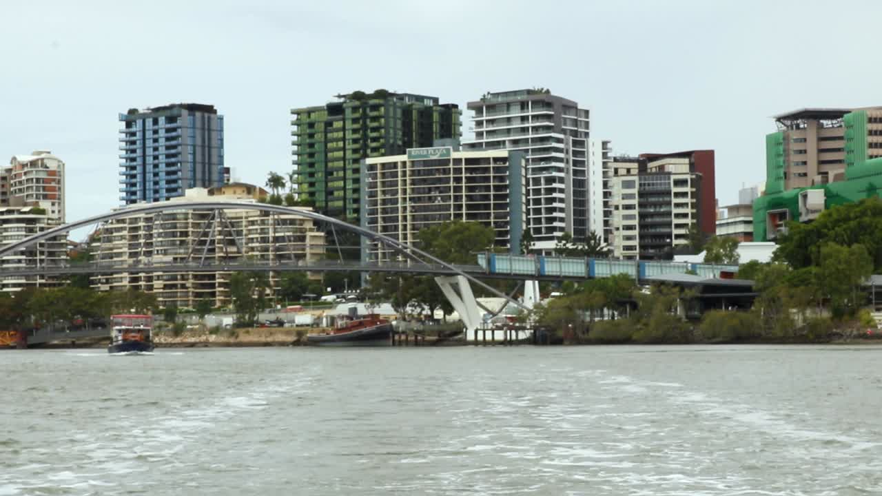 View from Brisbane River ferry of Goodwill Bridge and colourful buildings on an overcast day.