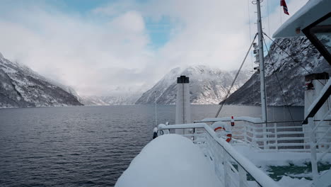 Slow-motion-POV-of-a-winter-ferry-boat-ride-in-Geirangerfjord-to-Geiranger,-Norway,-with-snowy-mountains-and-captivating-fjord-views