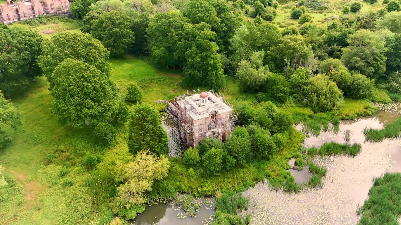 Aerial View of a Building with a Red Dome Under Renovation Amidst Lush Green Nature and Water