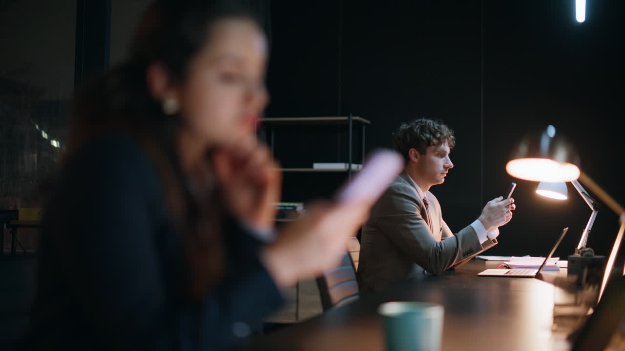 Professional woman texting smartphone in evening office at desk with man closeup