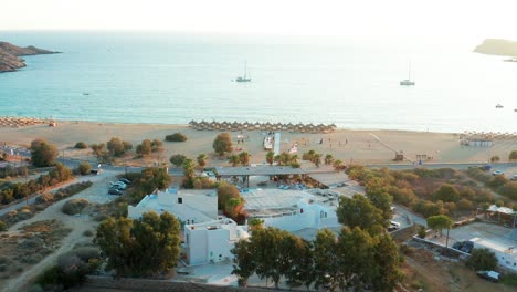 Aerial-flying-over-Beach-bar-at-Milopotas-Beach-Bright-sunlight-reflection-on-water,-Greece