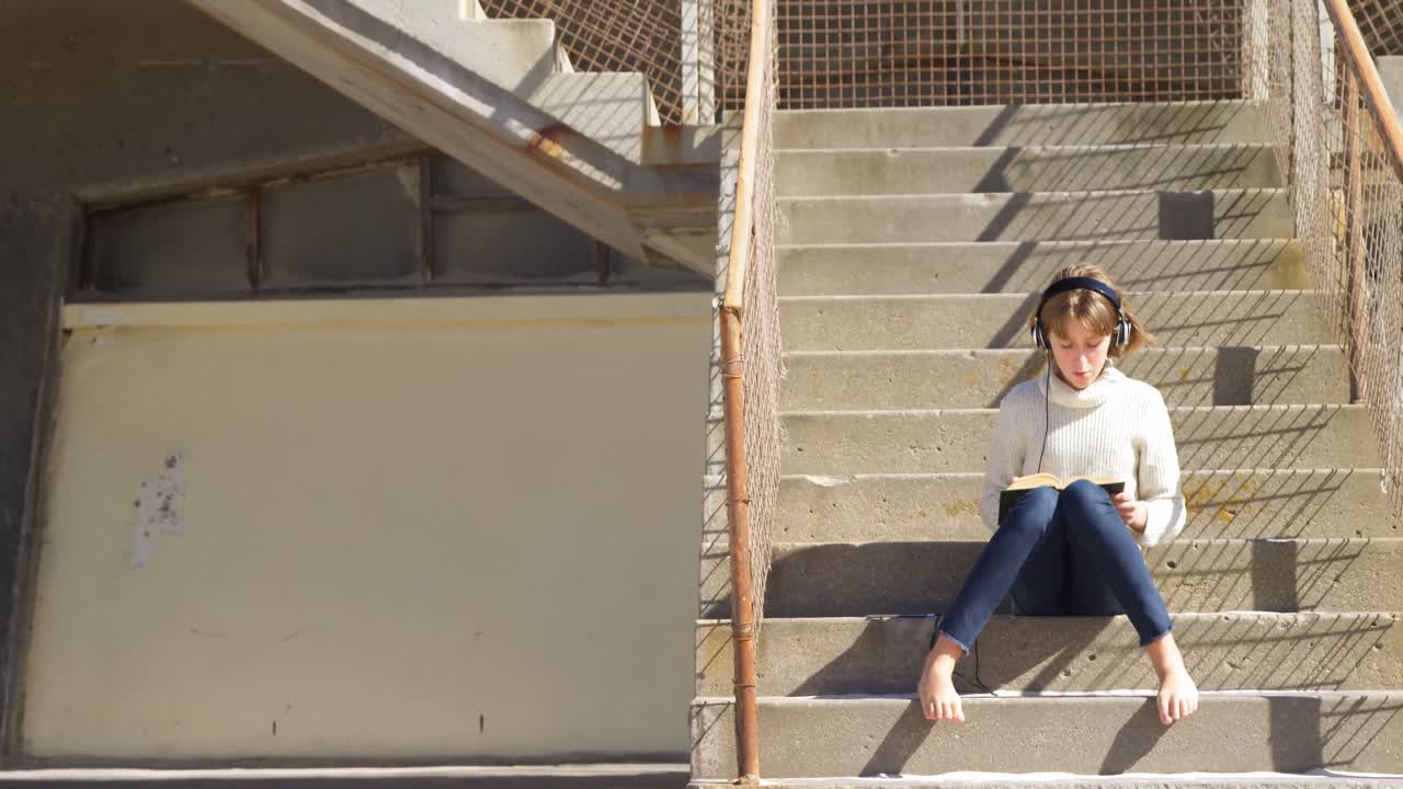 Girl listening music while reading a book at beach 4k