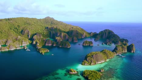 Wide-view-of-Piaynemo-island-bay-in-Raja-Ampat-Indonesia-with-docking-pier-right-and-trimaran-boat-left,-Aerial-pan-left-shot