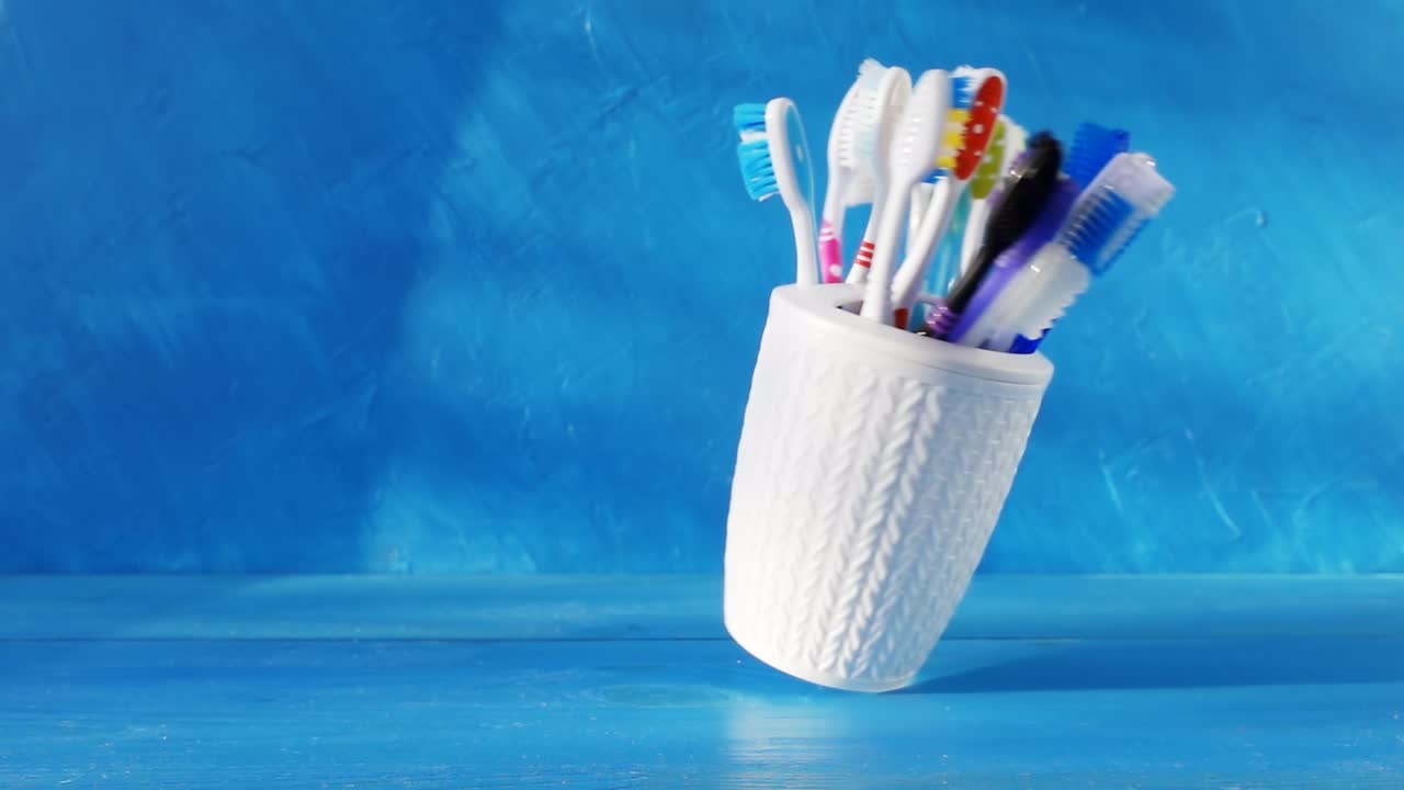 muchos cepillos de dientes diferentes en una taza blanca giran en una mesa contra un fondo azul. video de bucle crudo creativo 4k. filmado en cámara de cine de alta velocidad, 1000 fps.