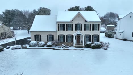 large house with beige siding covered in snow during flurries