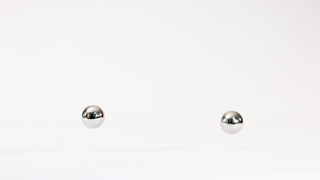 Chrome steel spheres fall, collide, and bounce across a bright white reflective studio background