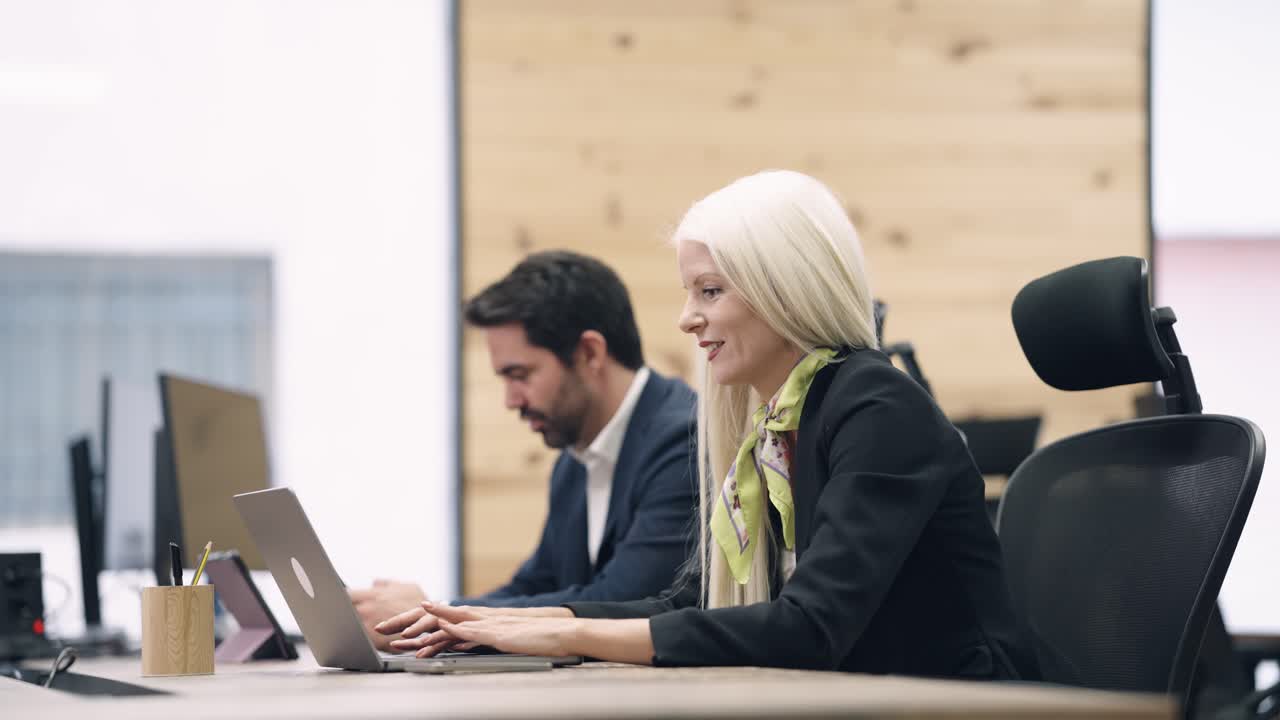 Donna d'affari sorridente che lavora al laptop in un ufficio moderno con un collega