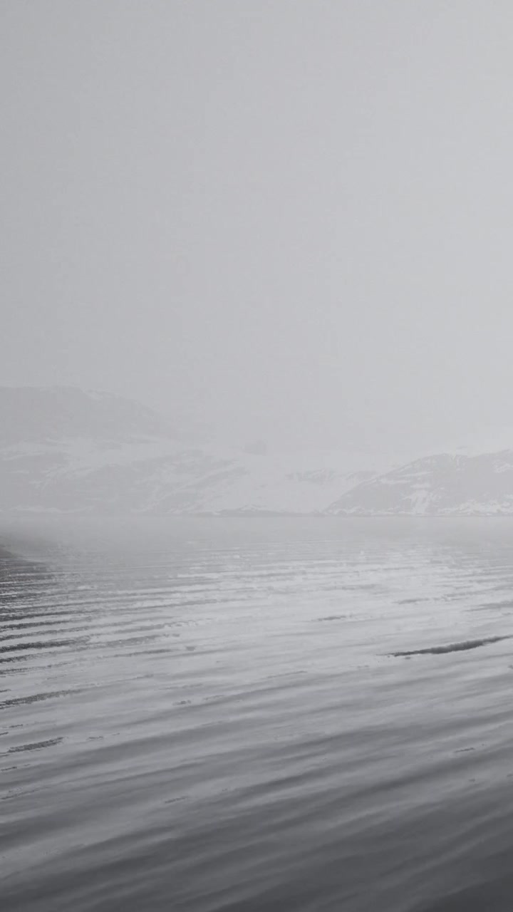 Fog covers a winter landscape with snow and distant trees near a river bank