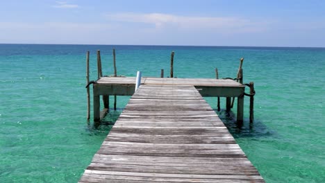 A-T-shape-pier-facing-the-open-ocean,-blue-skies,-green-ocean-Cropped