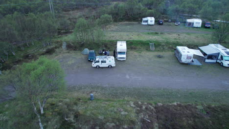 toma aérea de un campamento de caravanas con autocaravanas y camionetas estacionadas a última hora de la tarde y personas que preparan su campamento