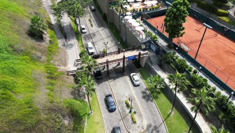 Stunning-tennis-club-discovered-by-an-aerial-drone-tilt-up-shot-in-the-middle-of-buildings,-palms,-trees,-historic-street-and-gardens