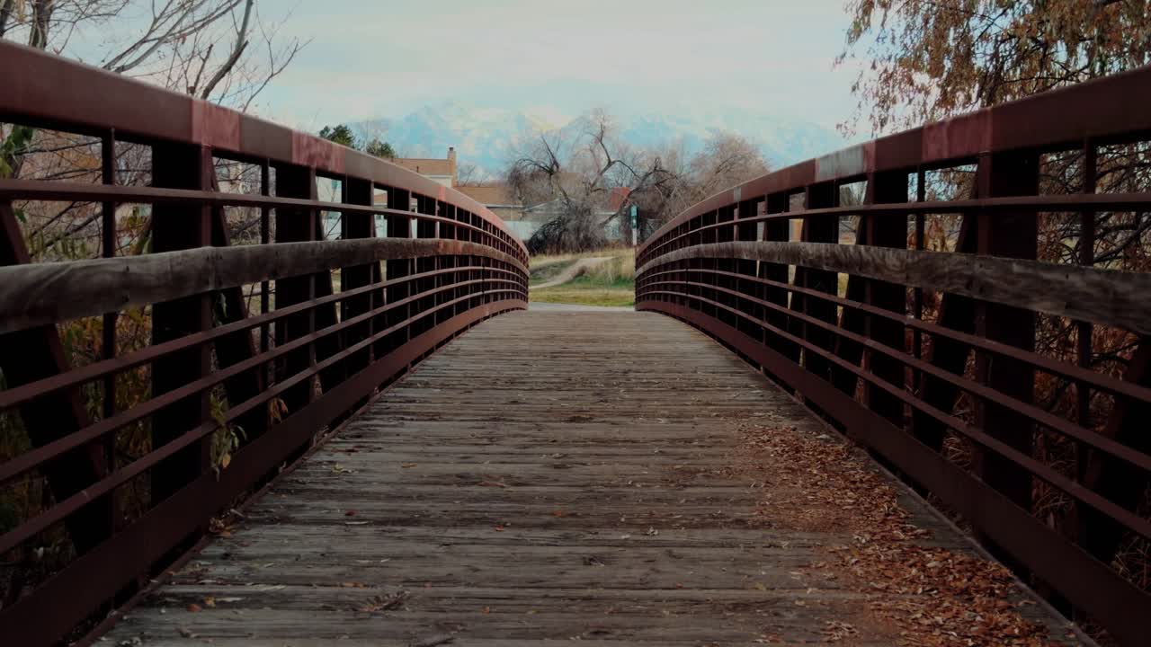 Bottom to top pan along a wooden pedestrian bridge surrounded by autumn trees and calm scenery