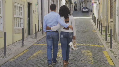 Back-view-of-young-couple-strolling-on-paved-street.